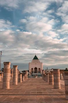 an empty courtyard with columns and a clock tower in the distance under a cloudy sky