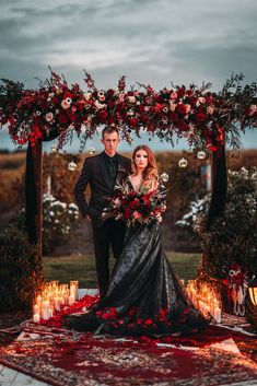 a man and woman are standing under an arch with flowers on it, surrounded by candles