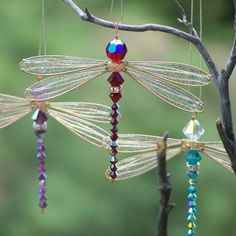 an image of three dragonflies hanging from a tree branch with beads attached to them