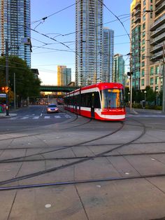 a red and white train traveling through a city next to tall buildings on a sunny day