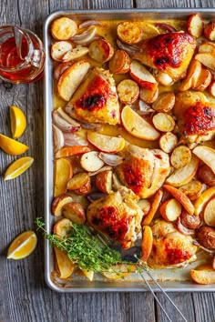 chicken, potatoes and carrots on a baking sheet with lemon wedges next to them