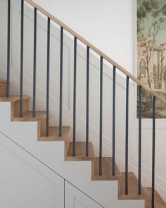 a stair case with metal handrails next to a white painted wall and painting on the wall