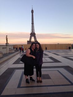 two women pose for a photo in front of the eiffel tower at sunset