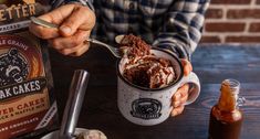 a person is holding a spoon in a mug with ice cream and chocolate cake inside