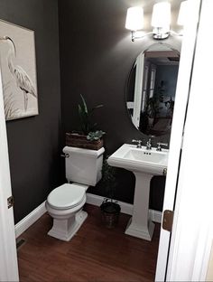 a white toilet sitting next to a sink in a bathroom under a large round mirror