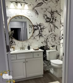 a bathroom with floral wallpaper and white vanity, toilet and sink area is shown