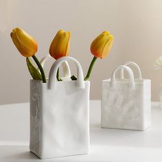 three yellow tulips in a white bag on a table next to a vase