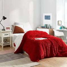 a bed with a red blanket on top of it in a bedroom next to a desk