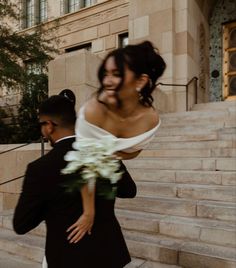 a bride carrying her groom down the stairs in front of a building on their wedding day