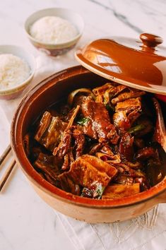 a bowl filled with meat and vegetables on top of a table next to bowls of rice