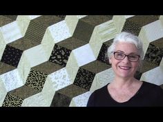 an older woman with glasses standing in front of a quilted wall hanging on the wall