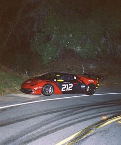 a red race car with numbers on it driving down the road at night time,