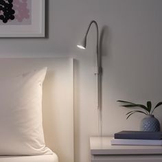 a bed with white sheets and pillows next to a wall mounted lamp on the headboard