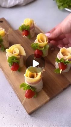 a person is making small appetizers on a cutting board with cheese and tomatoes