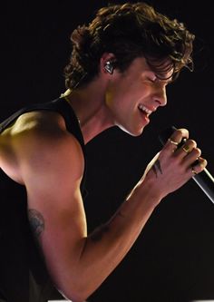 a shirtless man holding a microphone in his right hand and singing into the microphone