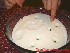 someone is pointing at some food in a glass bowl with white liquid and green sprinkles