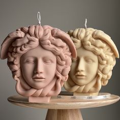 two ceramic head ornaments sitting on top of a wooden stand