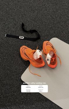 an orange sneaker is sitting on top of a white mat next to a black lanyard