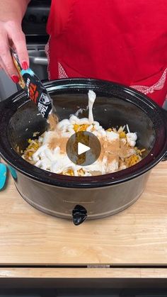 a person in an apron is adding ingredients to a crock pot