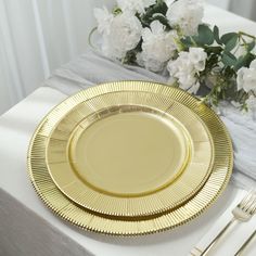 a gold plate sitting on top of a table next to white flowers and silverware