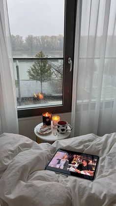 a bed with white sheets and two candles on top of it next to a window