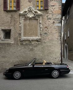 a black convertible car parked in front of a stone building with shutters on the windows