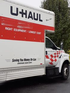 a moving truck parked on the side of the road in front of some bushes and trees