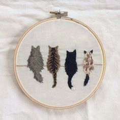 three different colored cats on a white background in a embroidery hoop with the cat's tail hanging down