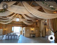 the inside of a barn decorated with white drapes and greenery on the ceiling