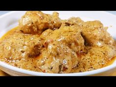 a white bowl filled with meat covered in gravy on top of a wooden table