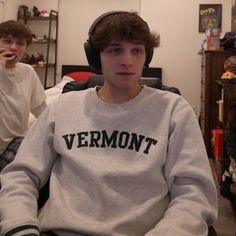 two young men sitting next to each other with headphones on their ears and one wearing a sweatshirt that says vermont