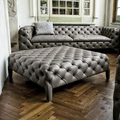 a large gray leather couch sitting on top of a wooden floor next to a window