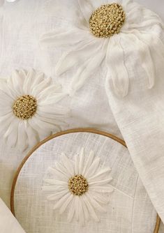 two white flowers are sitting on top of some linens and one is embroidered with gold thread