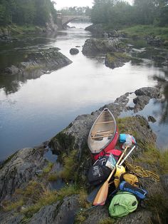 a canoe, kayak and backpacks are sitting on the edge of a river