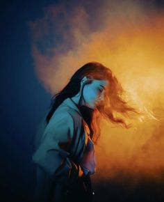 a woman with long hair standing in front of a yellow and blue background while blowing her hair