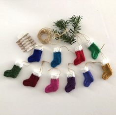 knitted christmas stockings hanging from string with pine tree branch in the middle and other decorations on white background