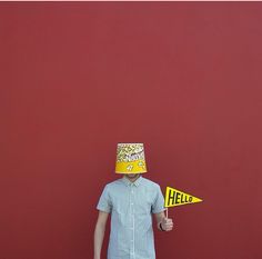 a person wearing a paper hat and holding a yellow sign in front of a red wall