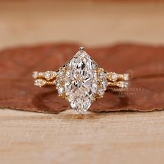 an oval cut diamond ring sitting on top of a wooden table next to a leaf