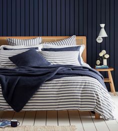 a bed with blue and white striped comforter on top of it next to a night stand