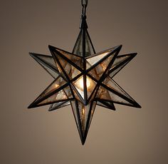 a moravian star hanging from a chain with lights inside it and on the ceiling in front of a wall