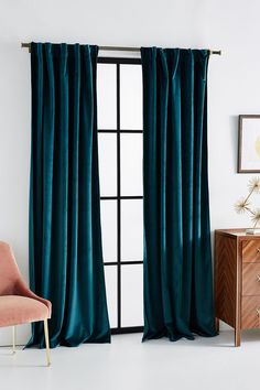 a living room with a chair and window covered in teal colored velvet drapes