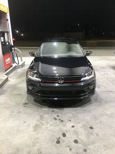 a black car is parked at a gas station with its hood open and it's lights on