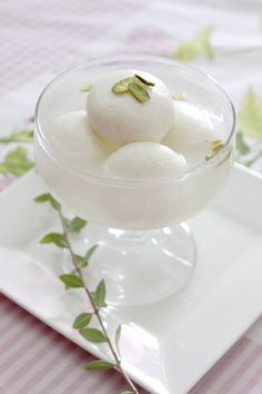 some food is in a glass bowl on a plate with green leaves and pink table cloth