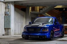 a blue pickup truck parked in a parking lot next to a building with stairs and railings