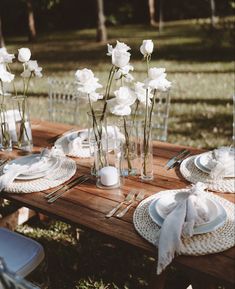 the table is set with white flowers in vases, plates and napkins on it