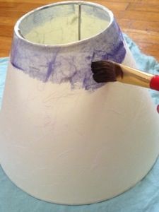 a person holding a paintbrush in front of a white lamp shade