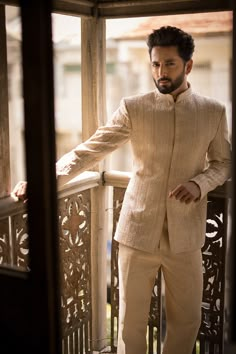 a man in a beige suit standing on a balcony