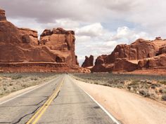 an empty road in the middle of desert with large rocks on both sides and cloudy sky above