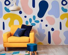 a yellow chair sitting in front of a wall with colorful shapes painted on the walls