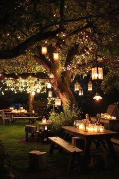 an outdoor dining area is lit up with candles and lanterns, while the tables are surrounded by trees